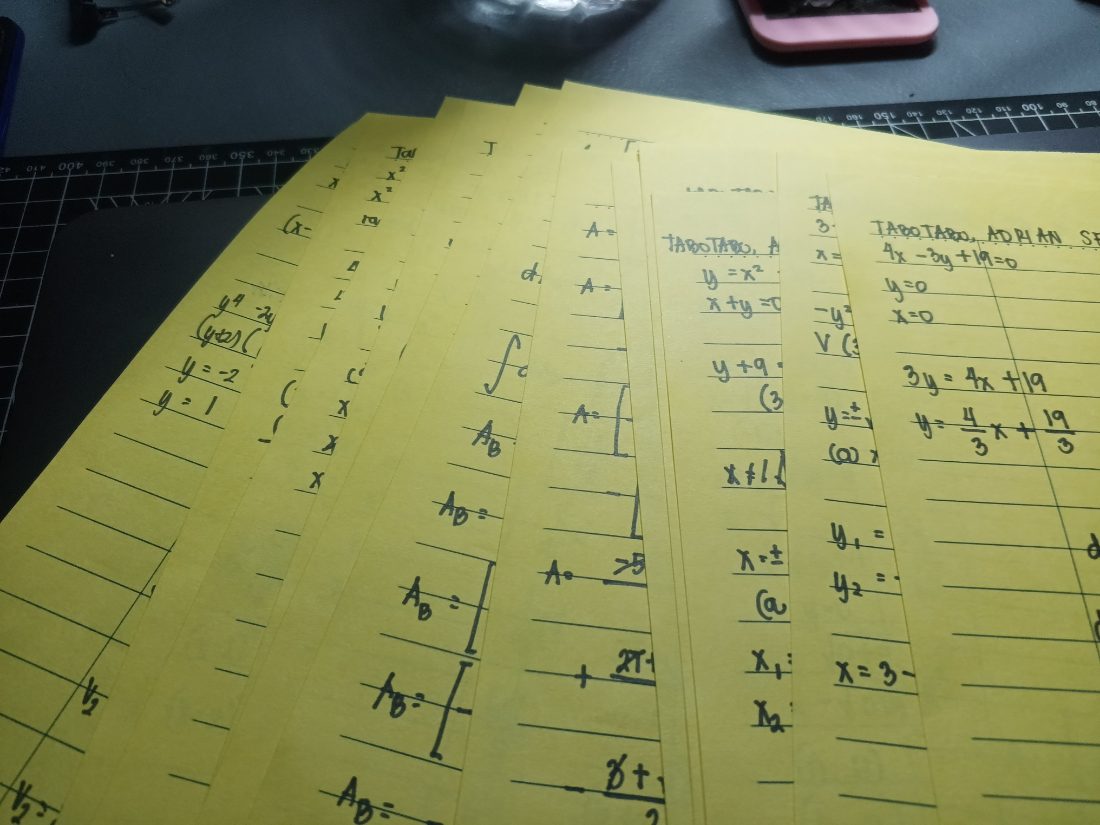 A fanned stack of handwritten yellow worksheets covered in integrals and areas between curves.